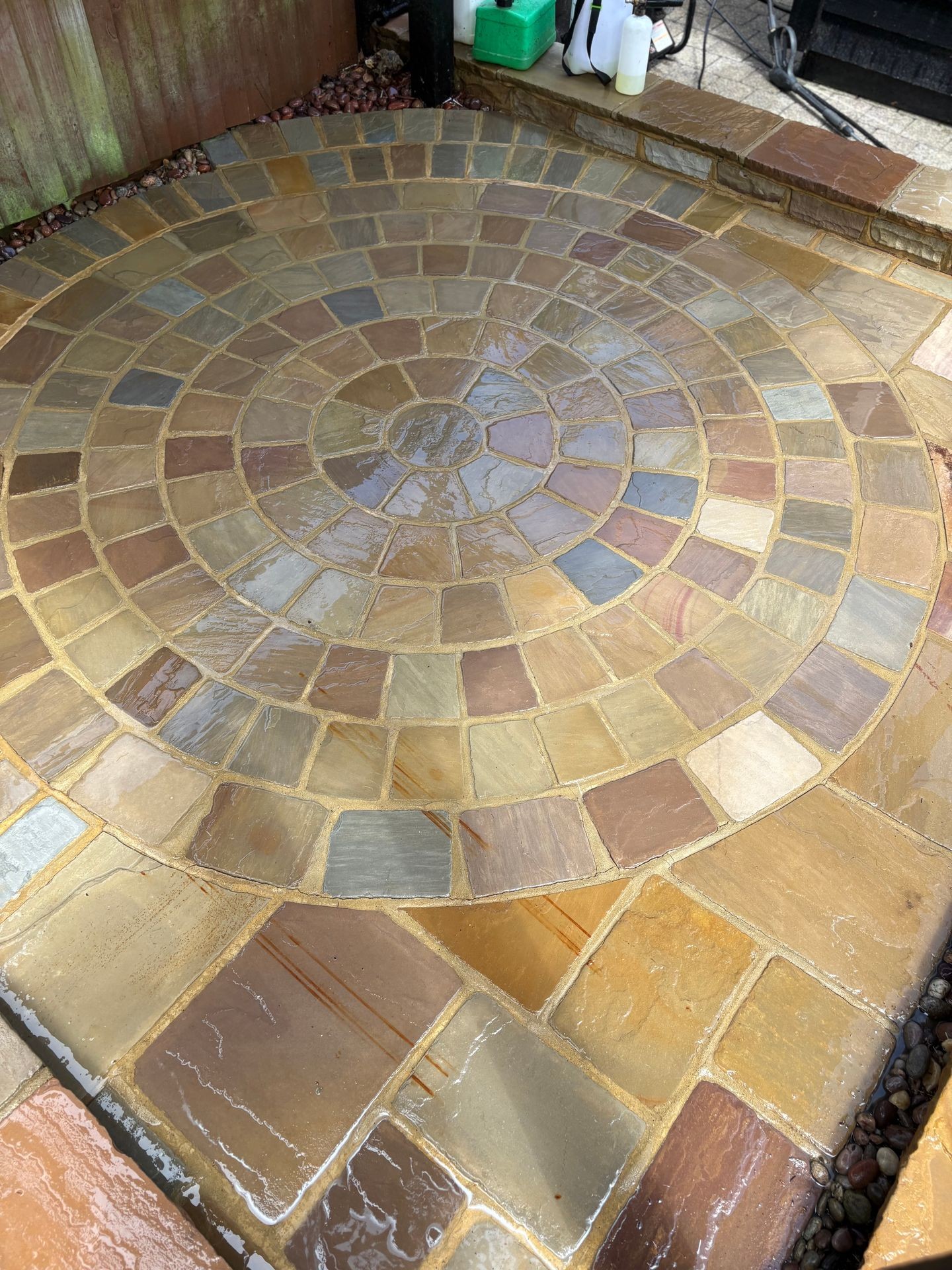 Circular stone patio with concentric rings of variously colored tiles, wet from recent cleaning.