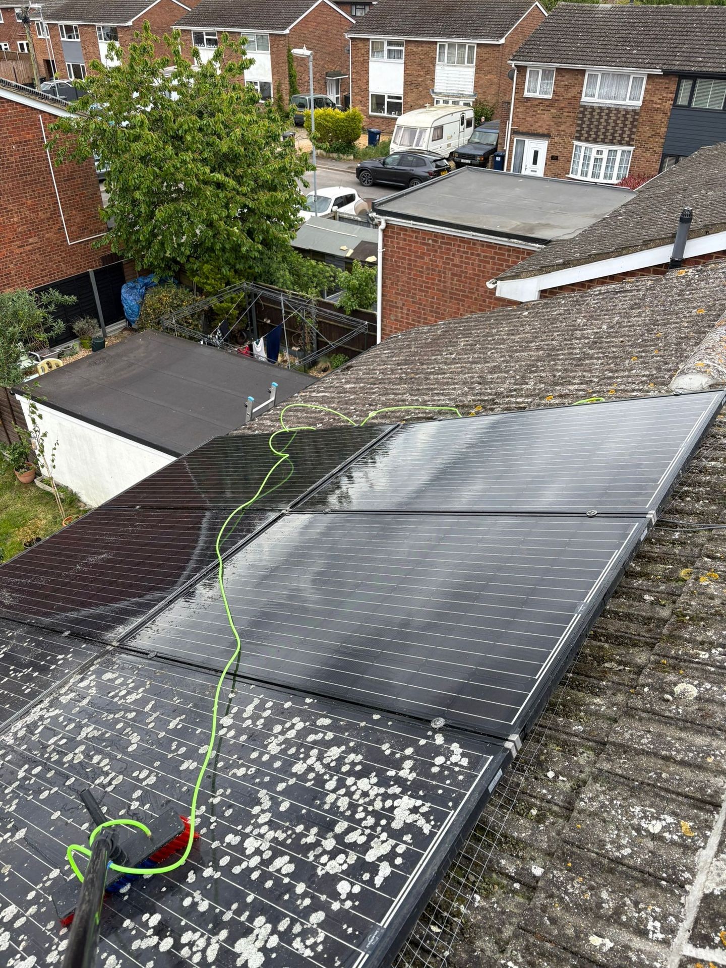 View of solar panels on a roof being cleaned with a brush, overlooking residential neighborhood.